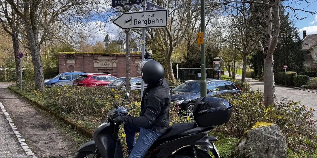 Alex auf dem Roller am Wegweiser zur Merkurbergbahn Baden-Baden